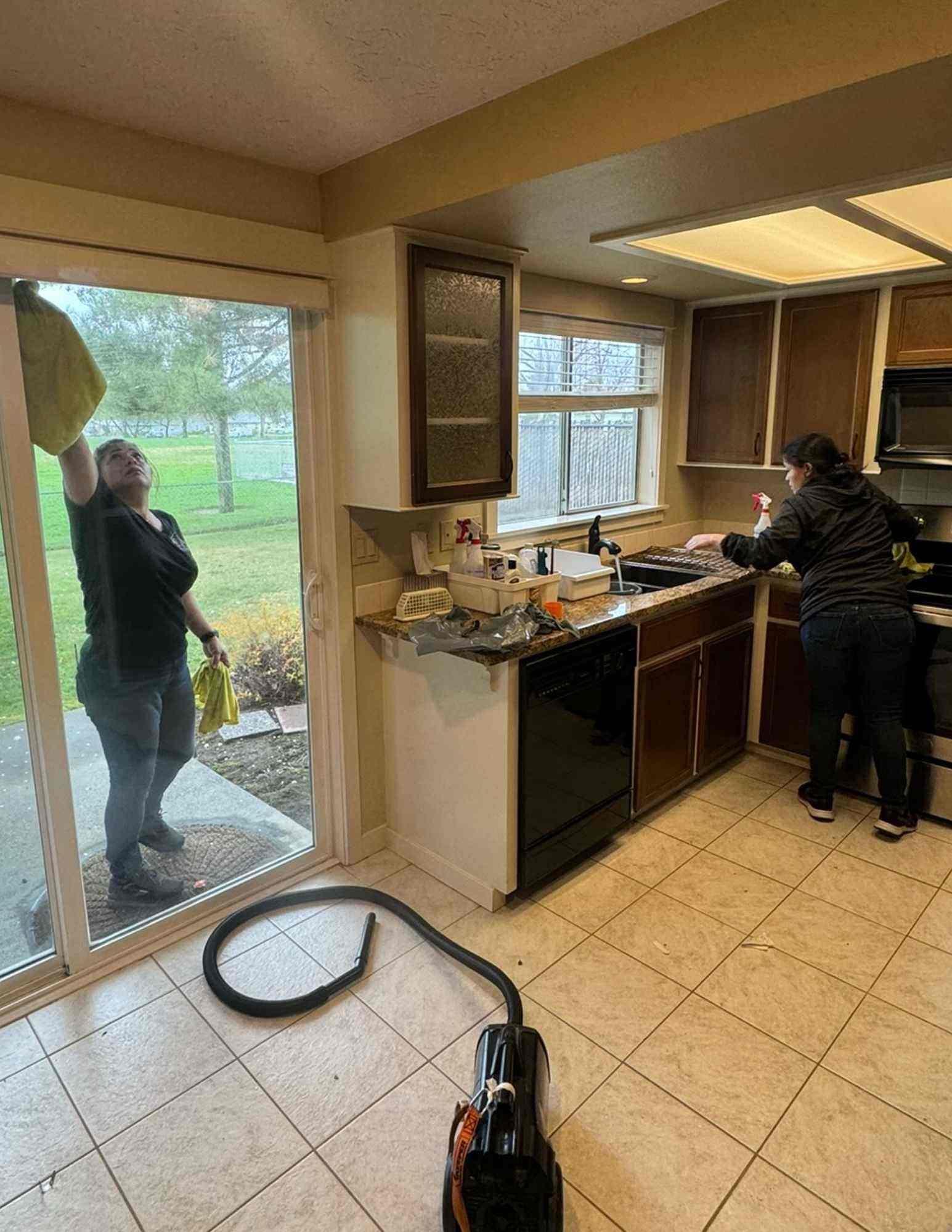 Professional cleaning team from DUO Cleaning Company diligently working in a kitchen, with one person cleaning a glass door and another washing countertops, reflecting thorough maid services in Richland, Kennewick, Pasco.